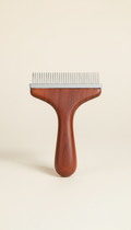 High-quality pet grooming comb centered against a neutral ivory background. The comb features polished metal teeth and a...